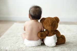 Back of a baby and teddy bear sitting together