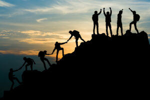A chain of people helping each other up onto a rock outcrop