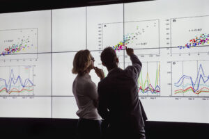 Two researchers discussing graphs on a large data display